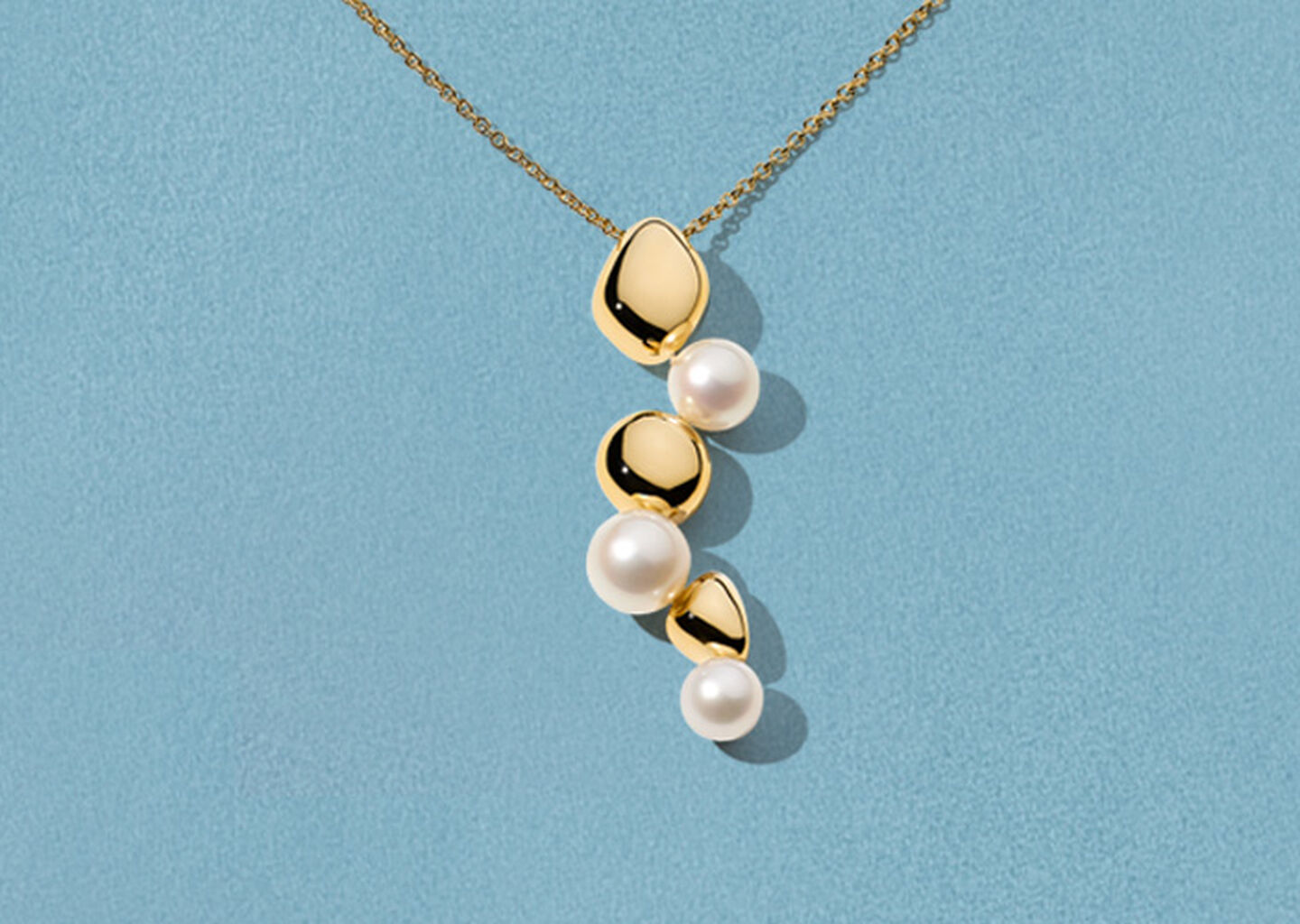 Collier Birks Pebble en or jaune avec perles sur un fond bleu.