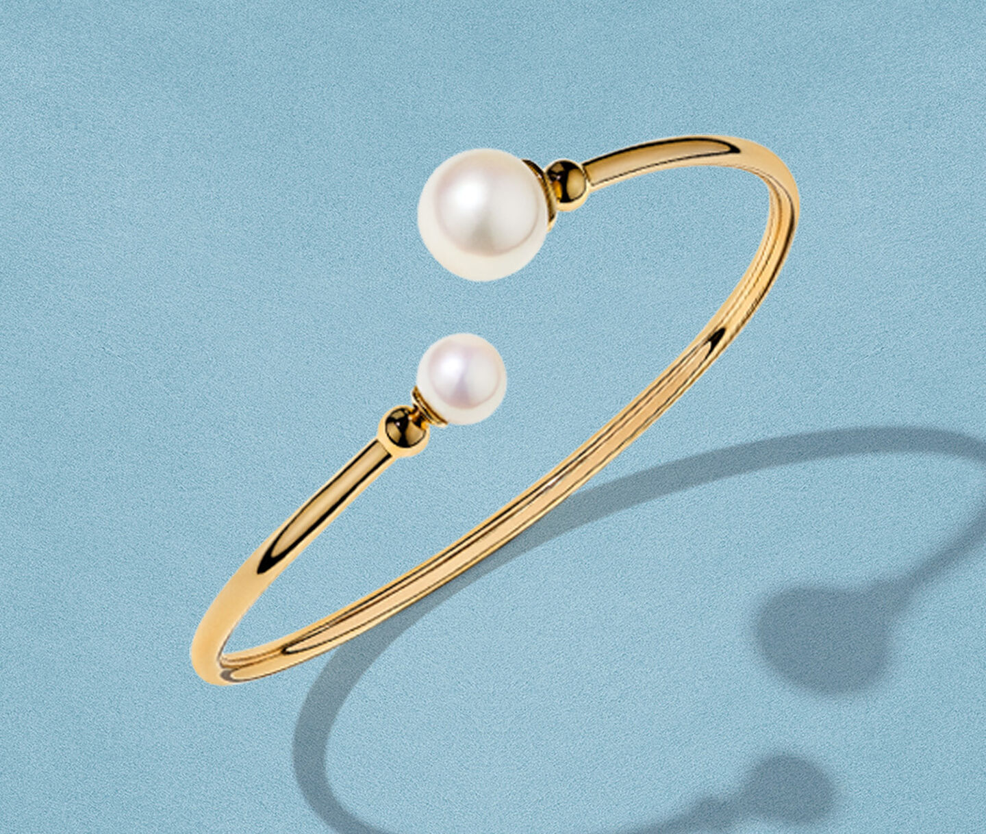 Birks Essentials pearl and gold bracelet on a blue background.