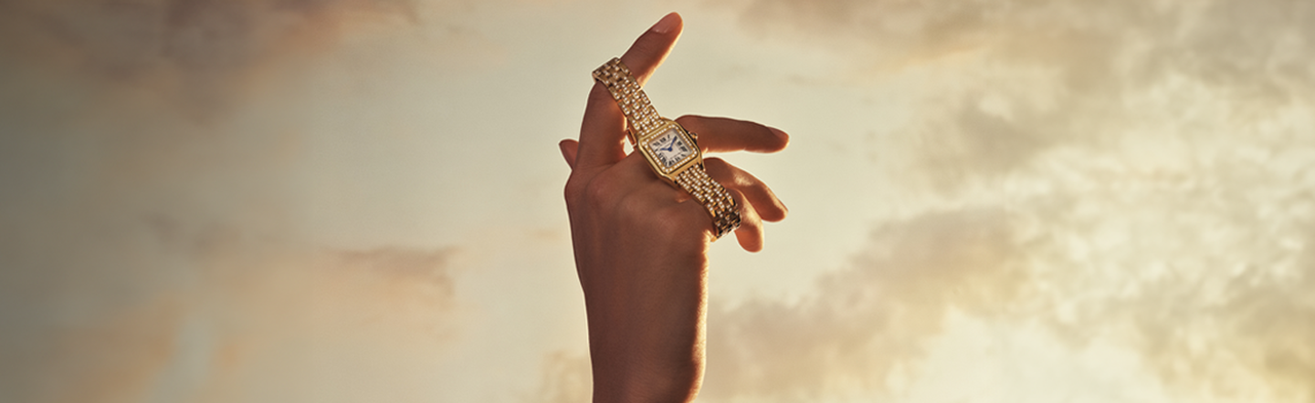 A woman holding a Panth&egrave;re de Cartier watch to the sky.
