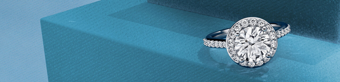 Birks 1879 diamond halo engagement ring with on a blue background.