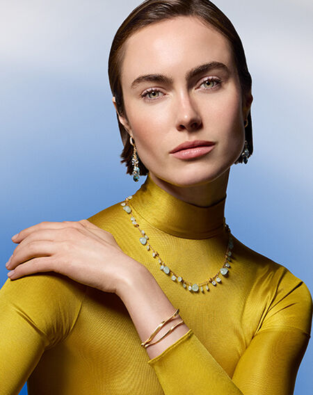 A woman wearing yellow gold jewellery on a blue background.