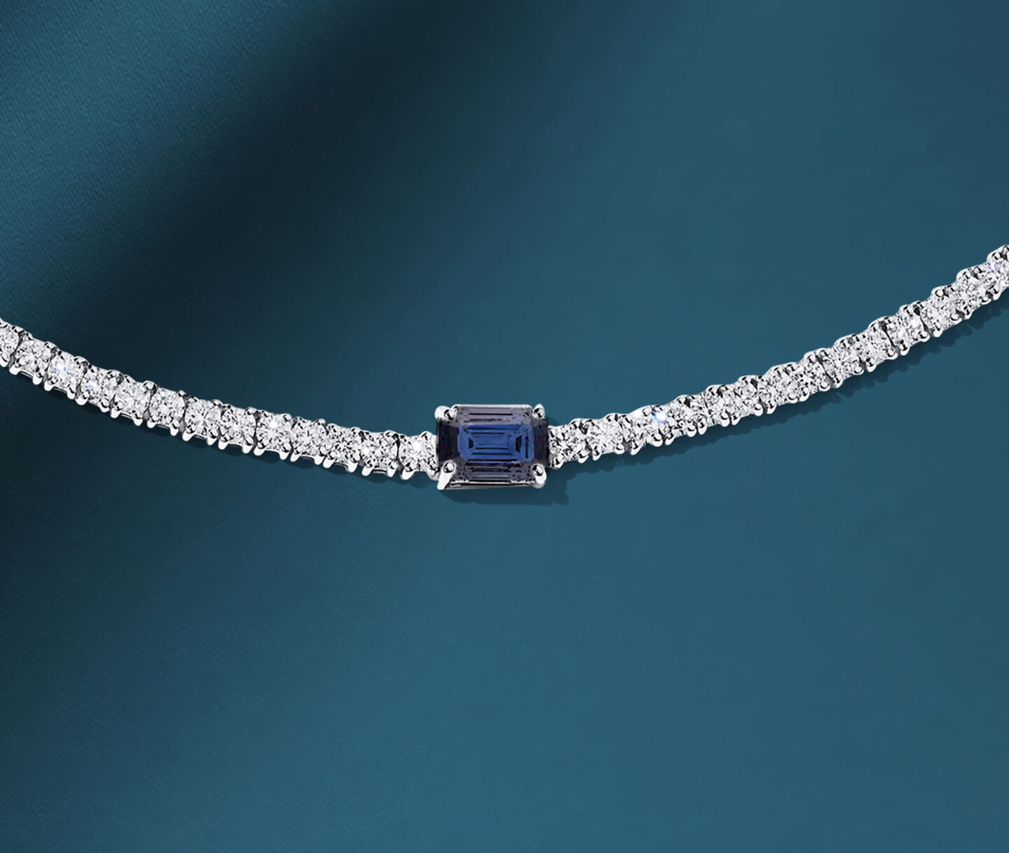 Birks Essentials sapphire and diamond tennis necklace on a blue background.