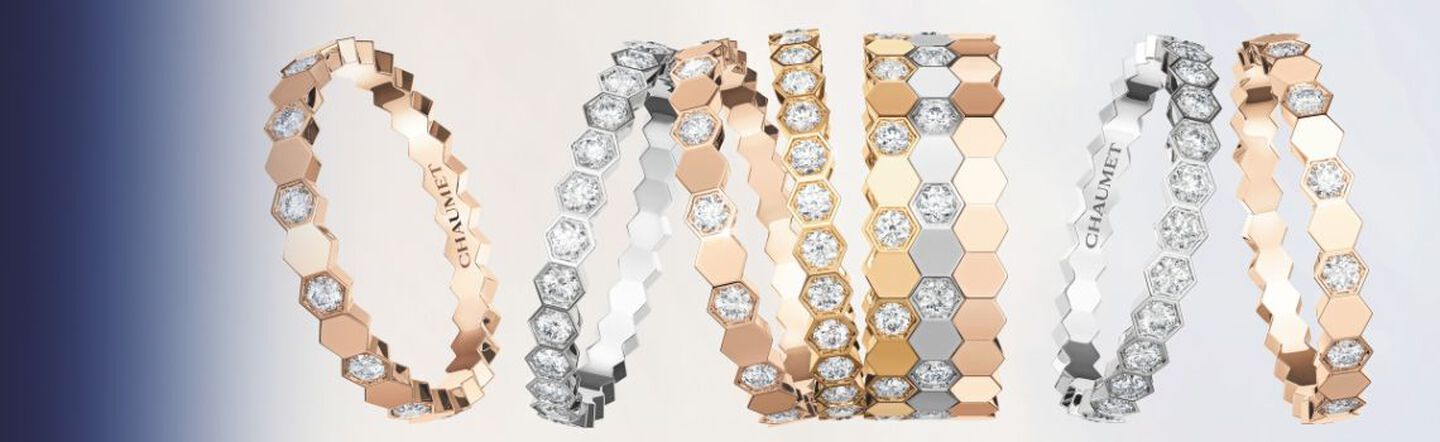 Hexagon-patterned diamond bracelets in rose, yellow, and white gold, elegantly arranged to spell “ONE” against a gradient blue-to-beige background, showcasing luxury and refined craftsmanship.