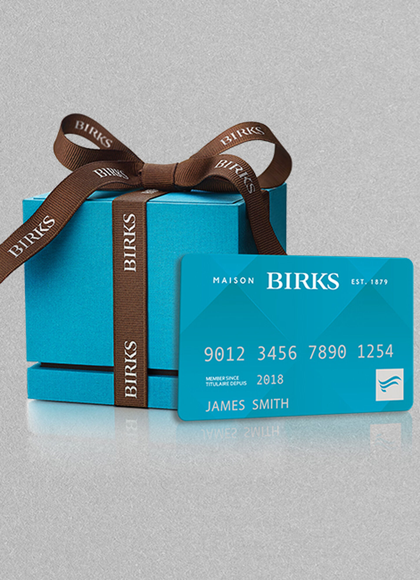 Boîte bleue emblématique de Maison Birks avec ruban brun et carte Flexiti de Maison Birks.