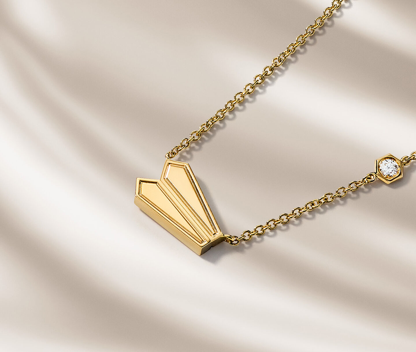 Birks Beekeeper yellow gold pendant necklace on a beige background.