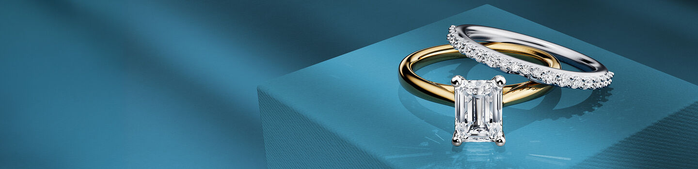 Birks 1879 diamond solitaire engagement ring with wedding band on a blue background.