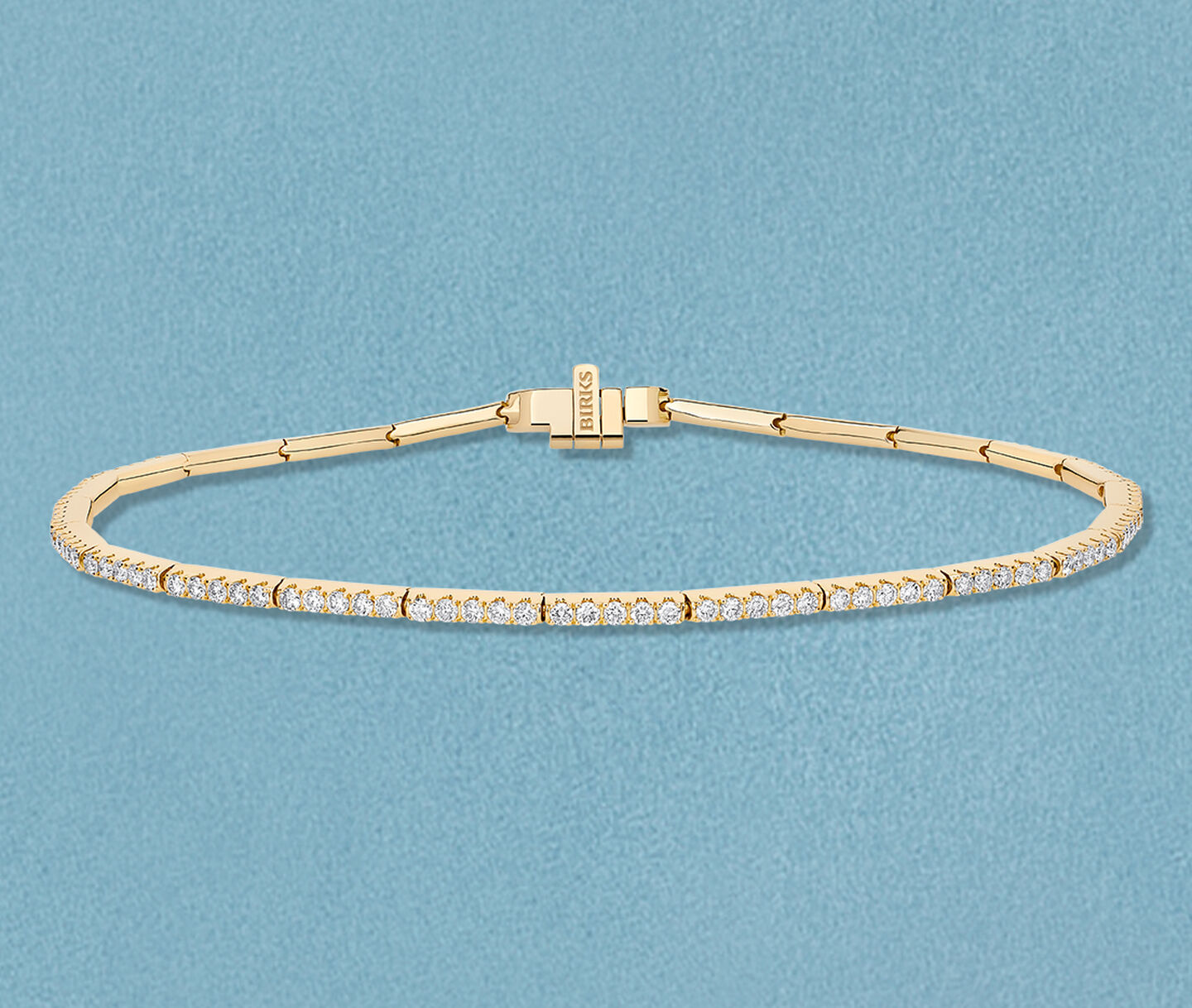 Birks Rosee du Matin diamond and yellow gold bracelet on a blue background.