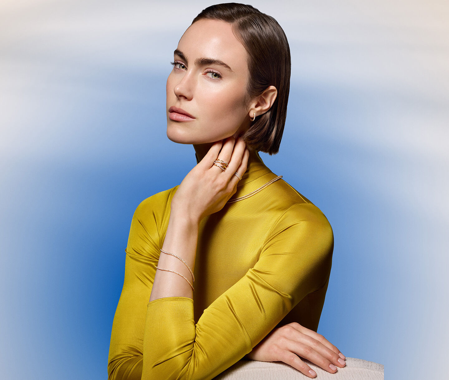 A woman wearing Birks diamond and yellow gold jewellery on a blue background.