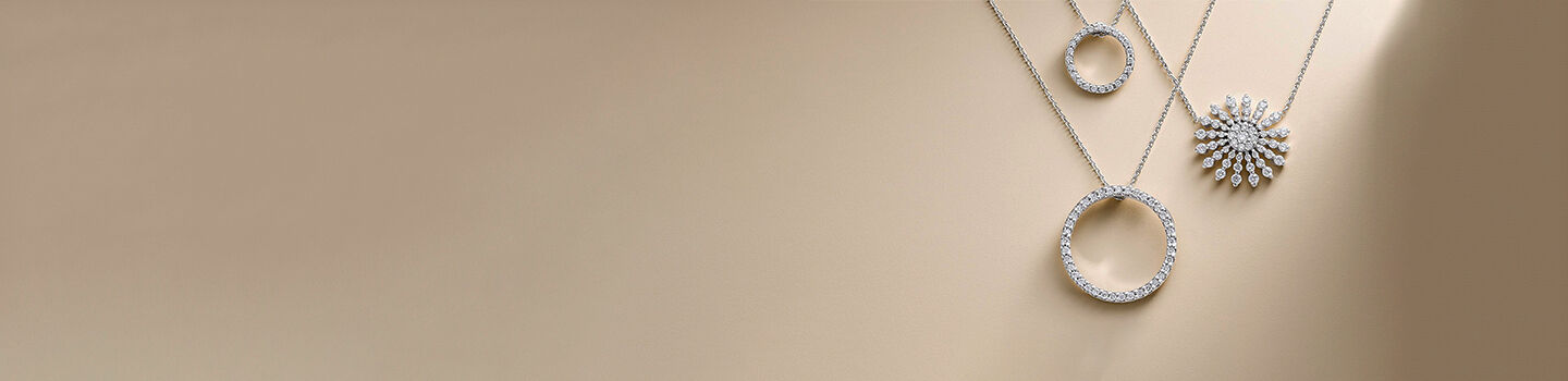 Three white gold and pendants from the Roberto Coin Tiny Treasures collection on a beige background.