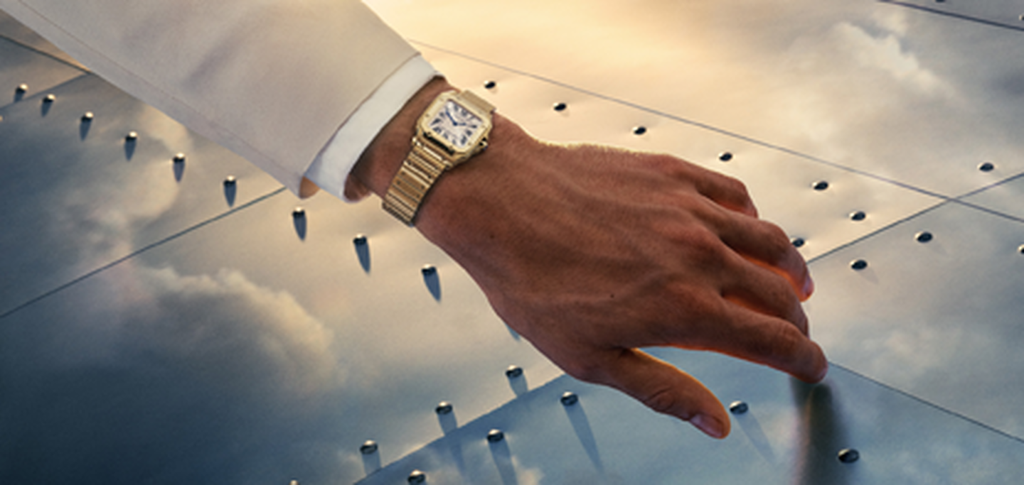 A man's hand wearing a Santos de Cartier watch.