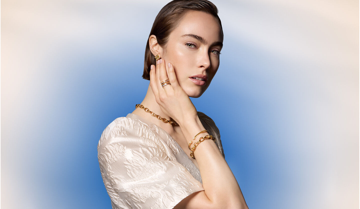 A woman wearing Birks and Roberto Coin jewellery on a blue background.