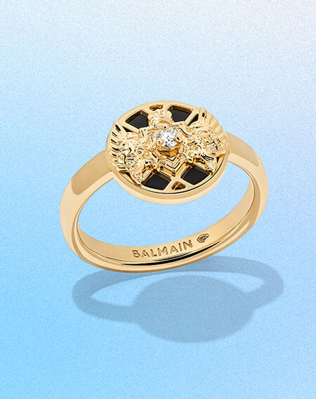 Bague Emblem par Balmain sur un fond bleu.