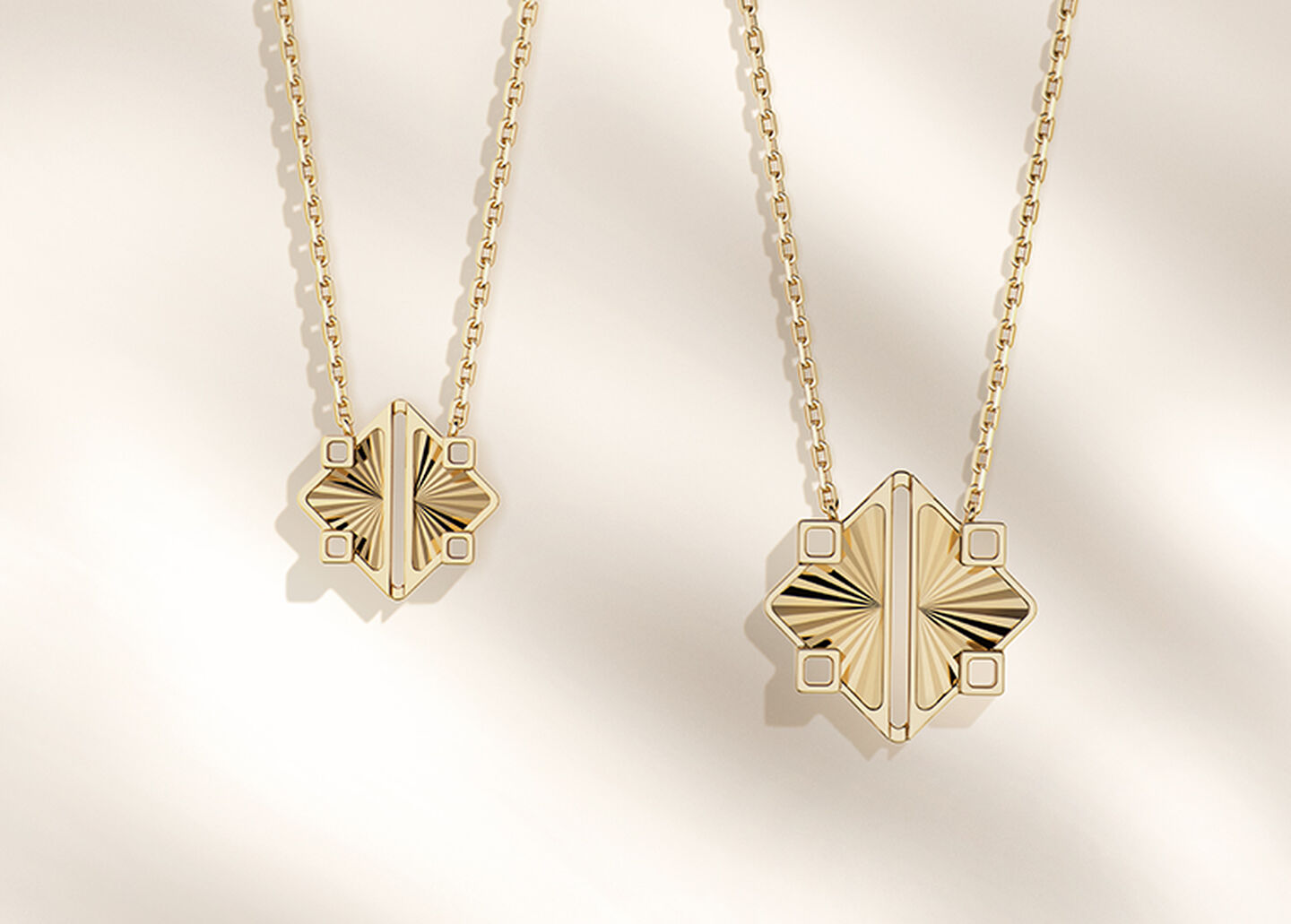 Two Birks Muse yellow gold pendant necklaces on a beige background.