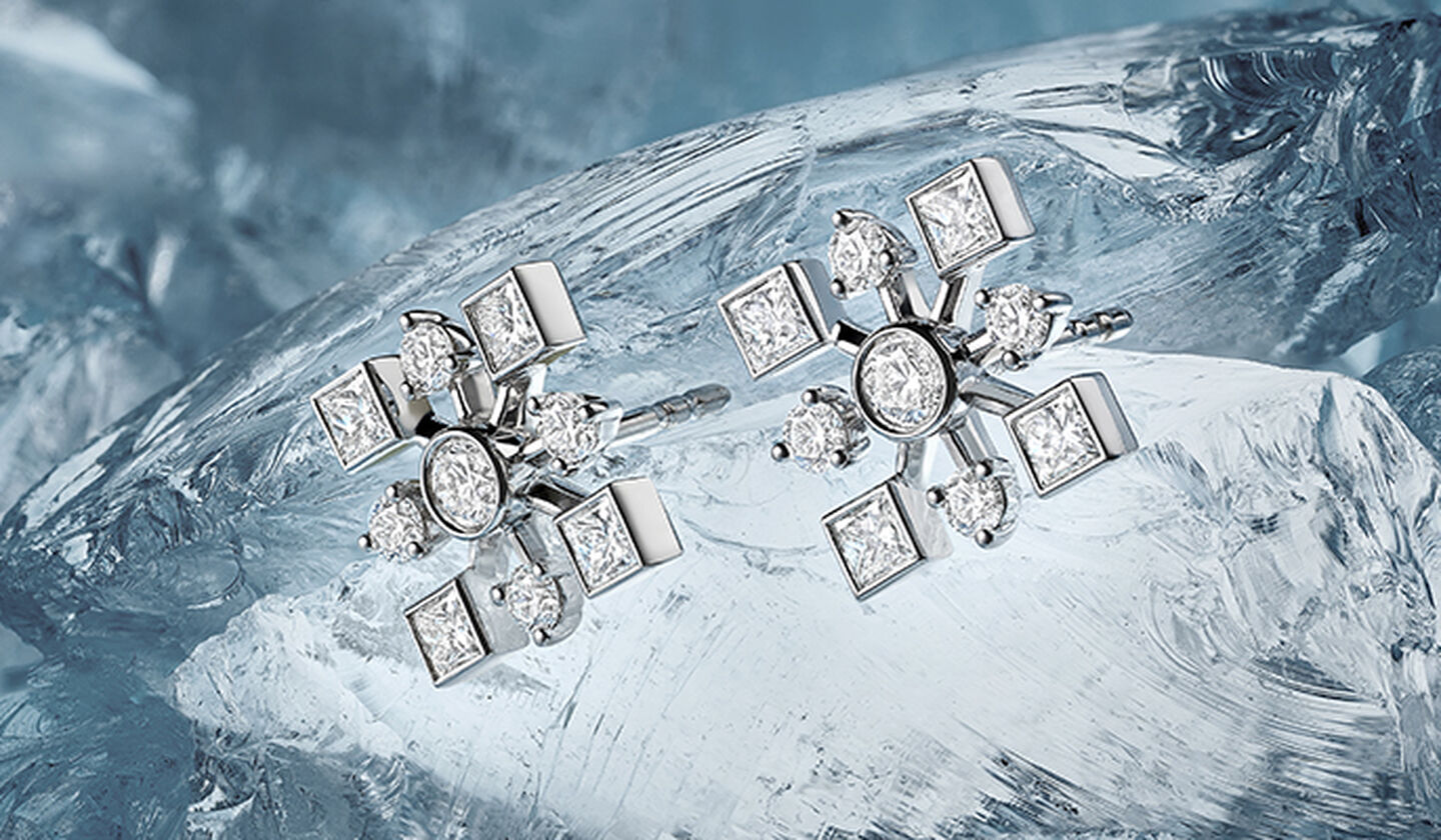 Boucles d'oreilles Birks Snowflake en or blanc et diamants sur fond blanc et bleu.