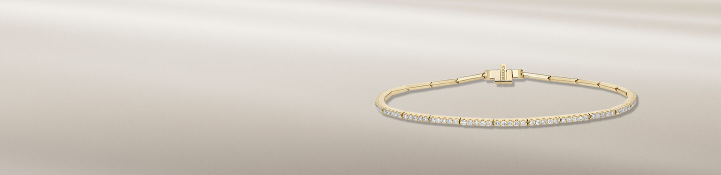 Bracelet Birks Essentiels avec diamants en or jaune sur un fond bleu.