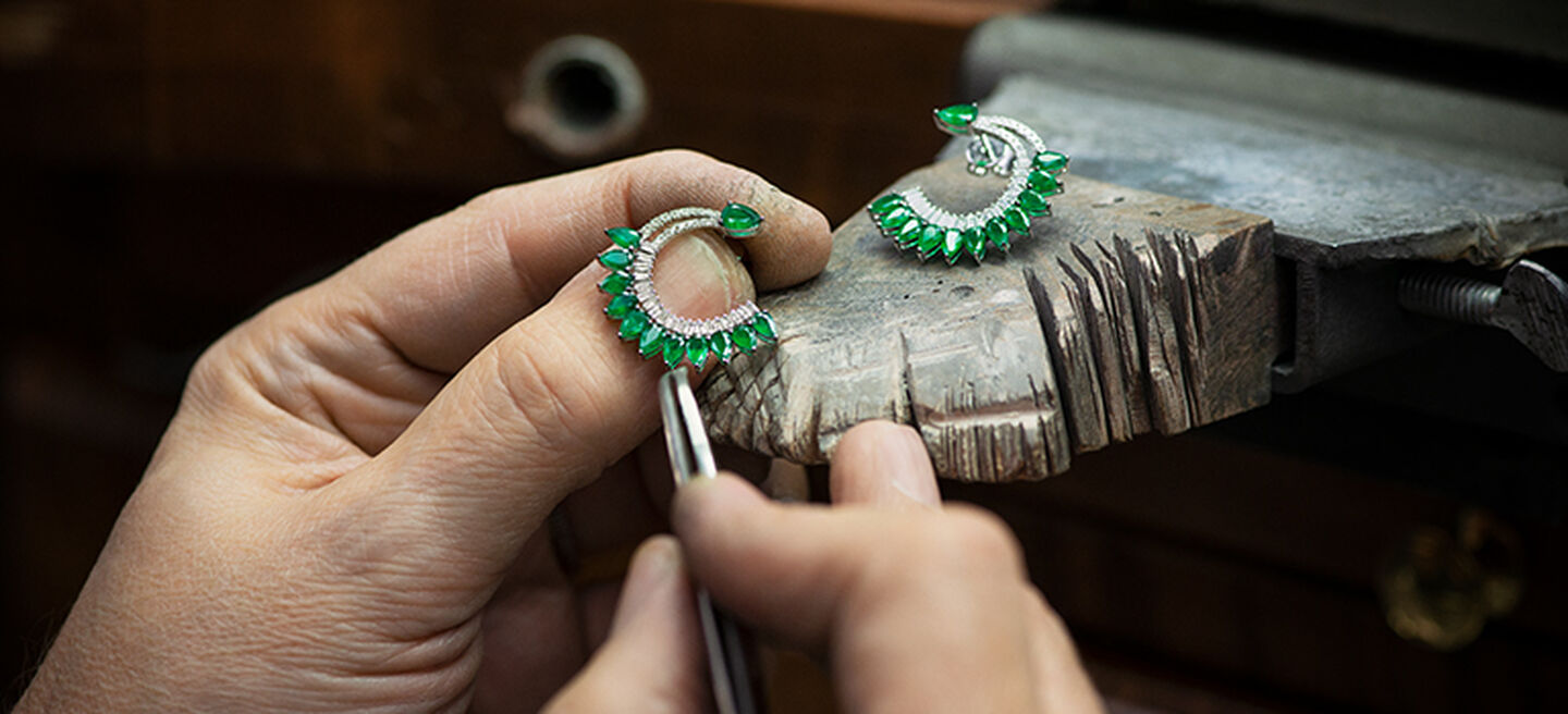 A jeweller carefully crafting a pair of emerald hoop earrings