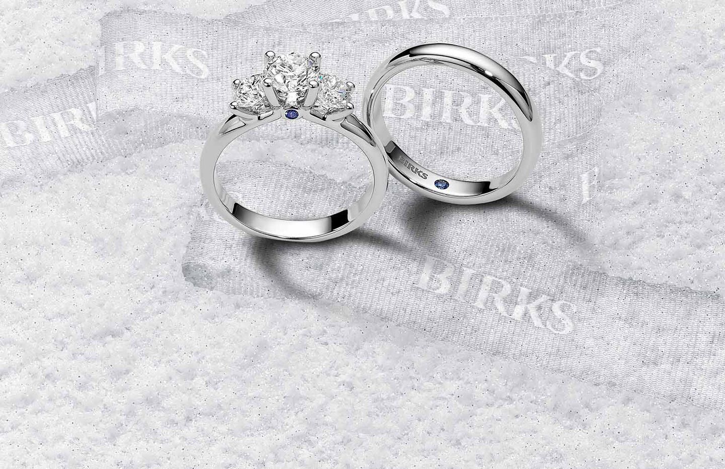 Birks Blue diamond engagement ring and wedding band with sapphire accents on a snowy background