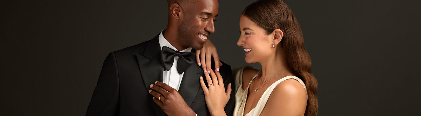 Elegant couple showcasing Birks engagement ring, gold wedding band, and fine jewellery including diamond earrings and necklace, perfect for weddings and special occasions.