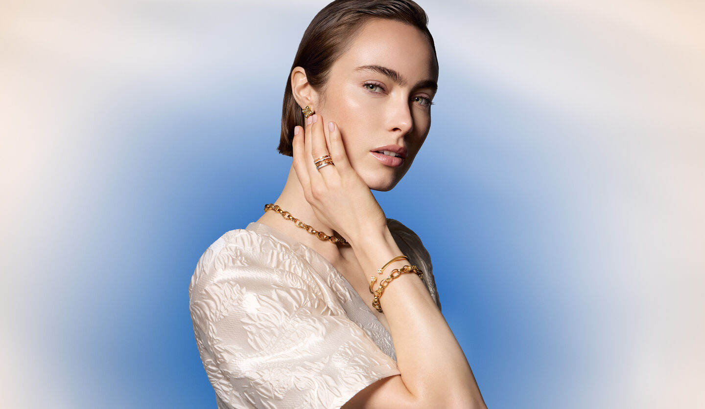 A woman wearing Birks and Roberto Coin jewellery on a blue background.