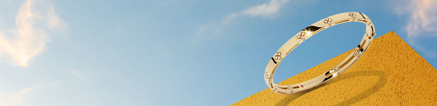 Bracelet Roberto Coin en or jaune sur pyramide orange et ciel bleu.