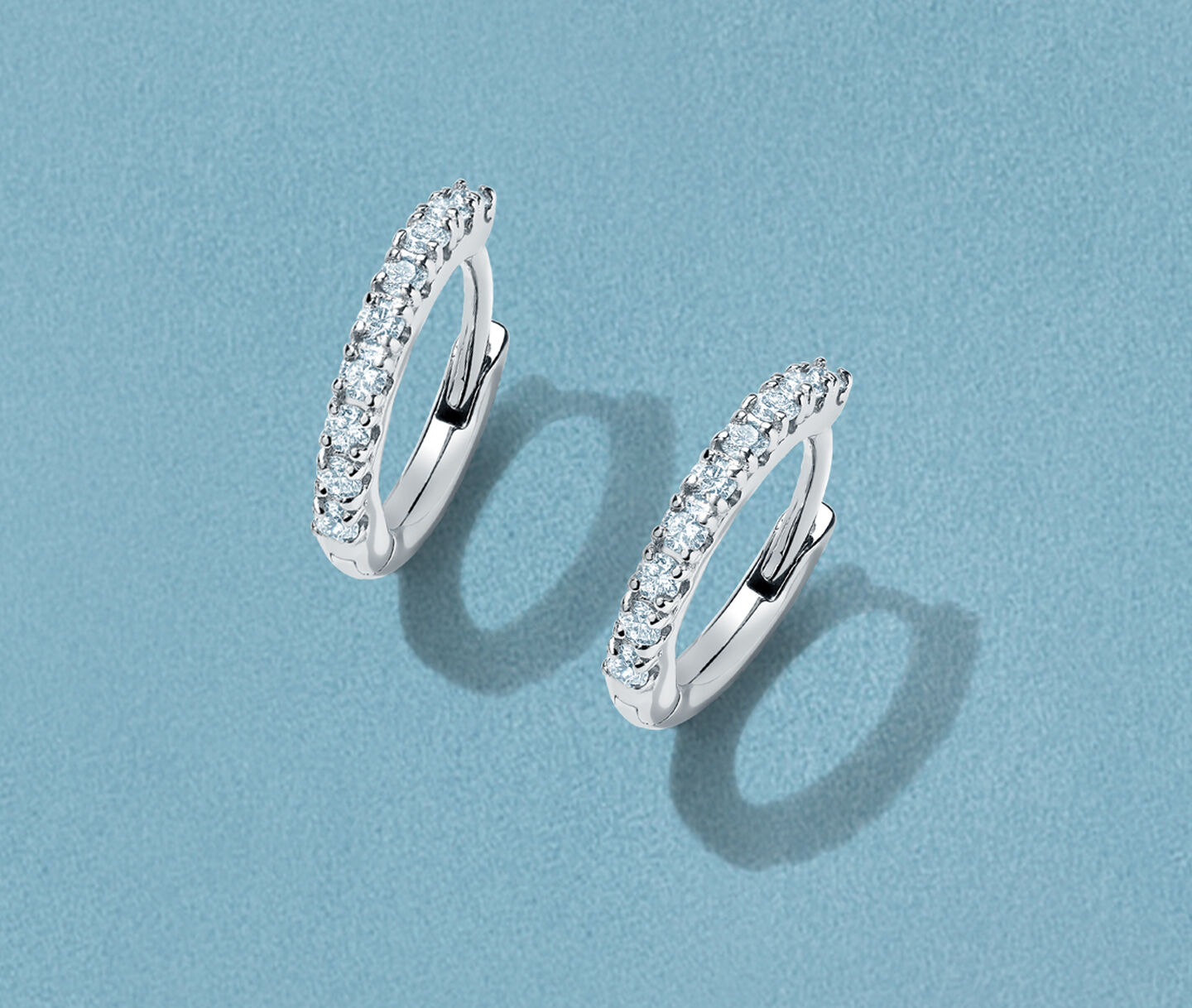 Boucles d'oreilles Birks Iconic Rosee du Matin avec diamants sur un fond bleu.