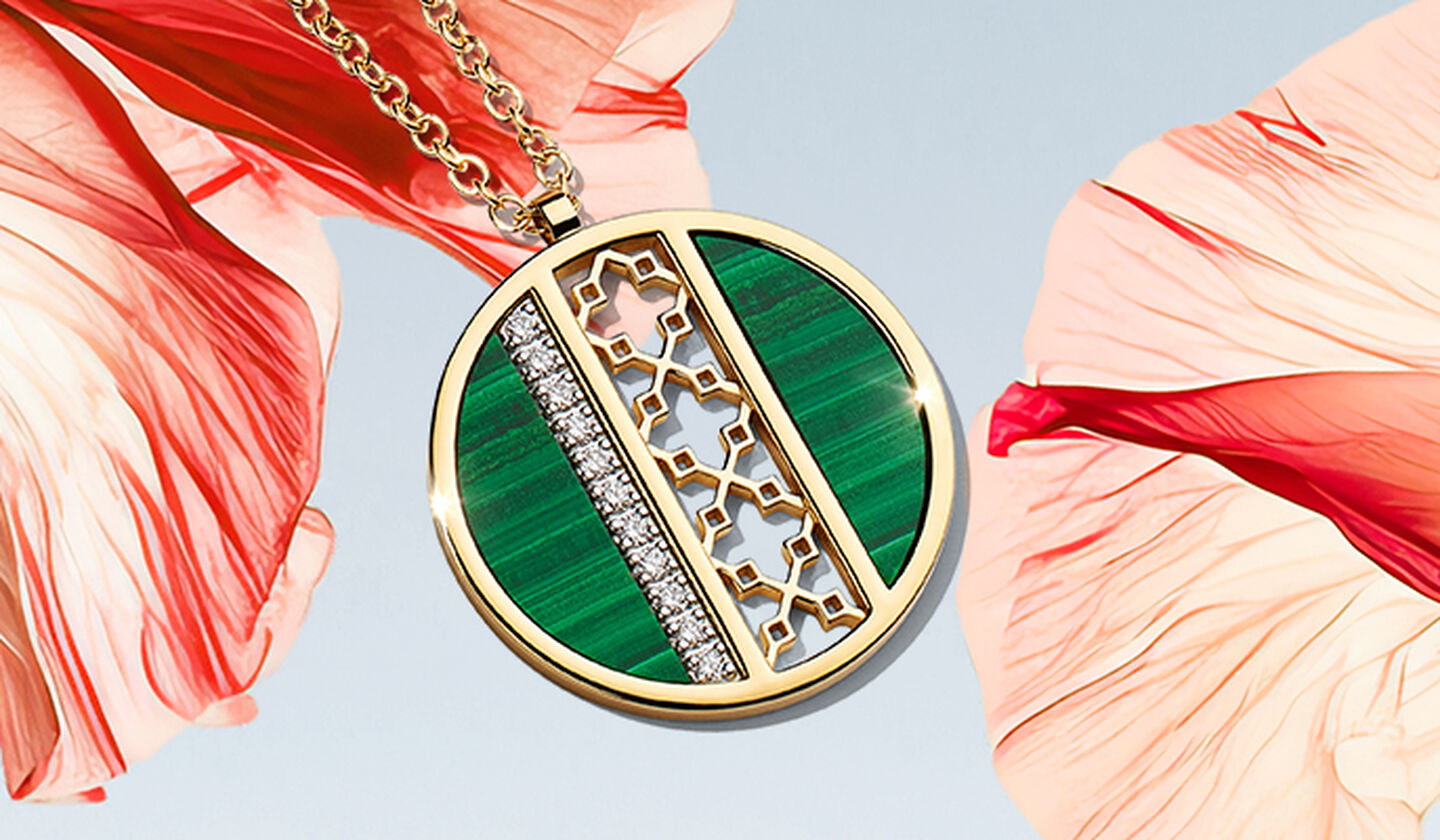  Un médaillon Birks Dare to Dream en malachite et diamants sur une fleur rouge-rose et fond bleu ciel clair.