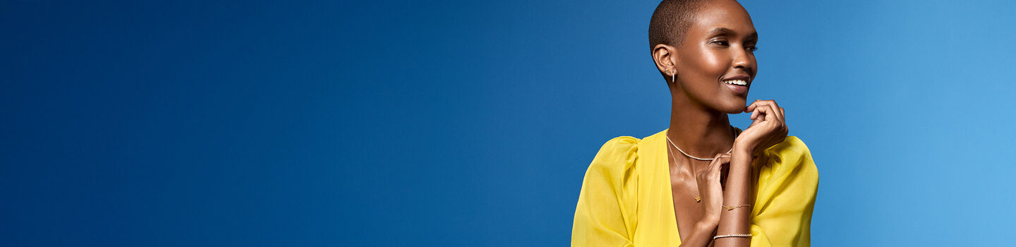 A woman wearing yellow gold jewellery from Maison Birks on a blue background.