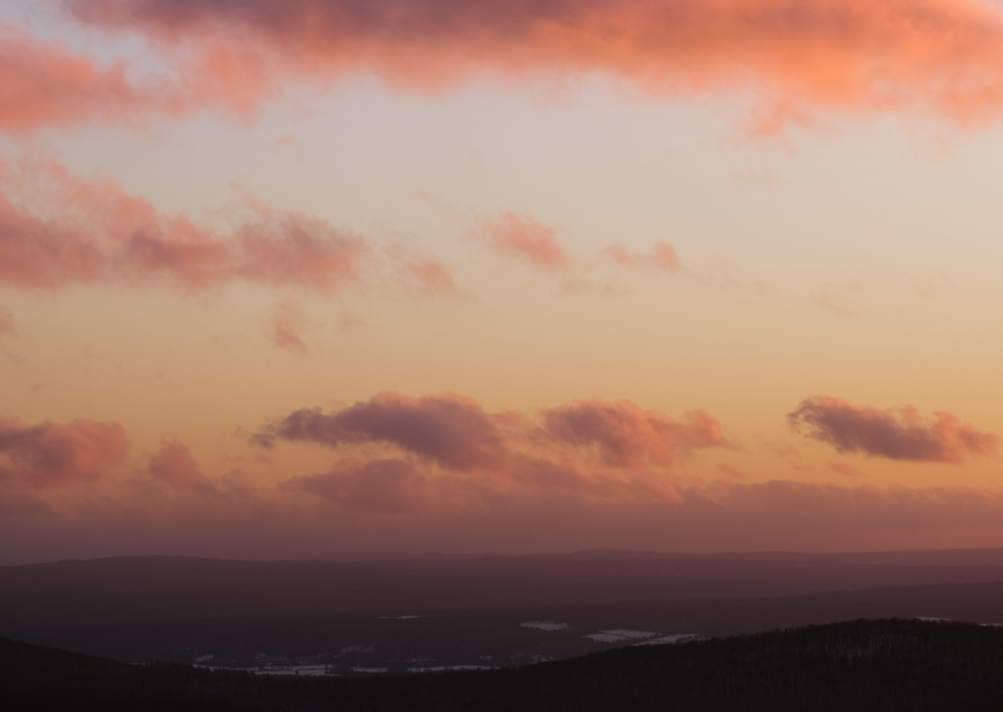 A sunset reflected in the clouds over snow covered mountains.