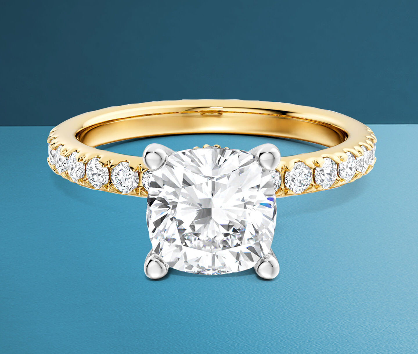 Birks Deco cushion-cut diamond engagement ring in yellow gold on a blue background.