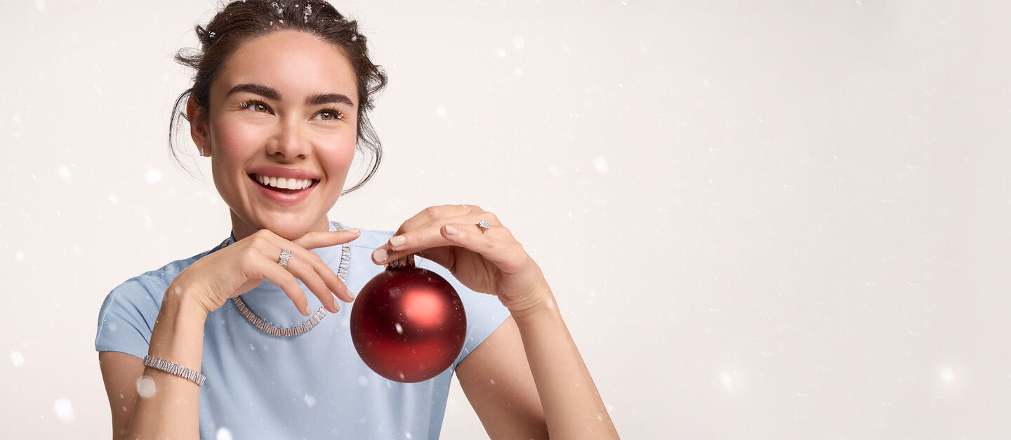 Person holding a red Christmas ornament, wearing a light blue shirt and Birks jewelry.