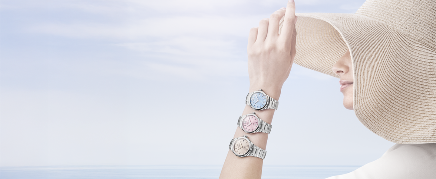 Une femme portant 3 montres Baume et Mercier centrées sur le poignet sur un fond bleu ciel.