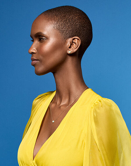 A woman wearing Birks Essentials opal necklaces and earrings on a blue background.