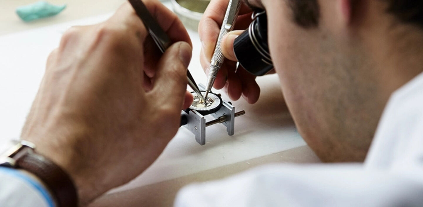 A watch specialist carefully repairs a watch on the table in front of him
