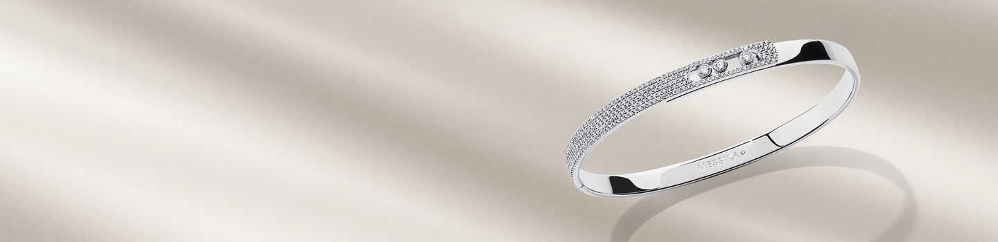 Messika Move Noa white gold and diamond bangle on a beige background.