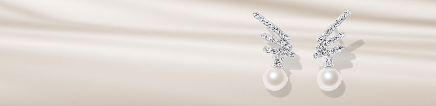 Yoko London pearl and diamond earrings on a beige background.