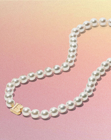 Birks Pearls strand necklace on a pinkish-yellow background.