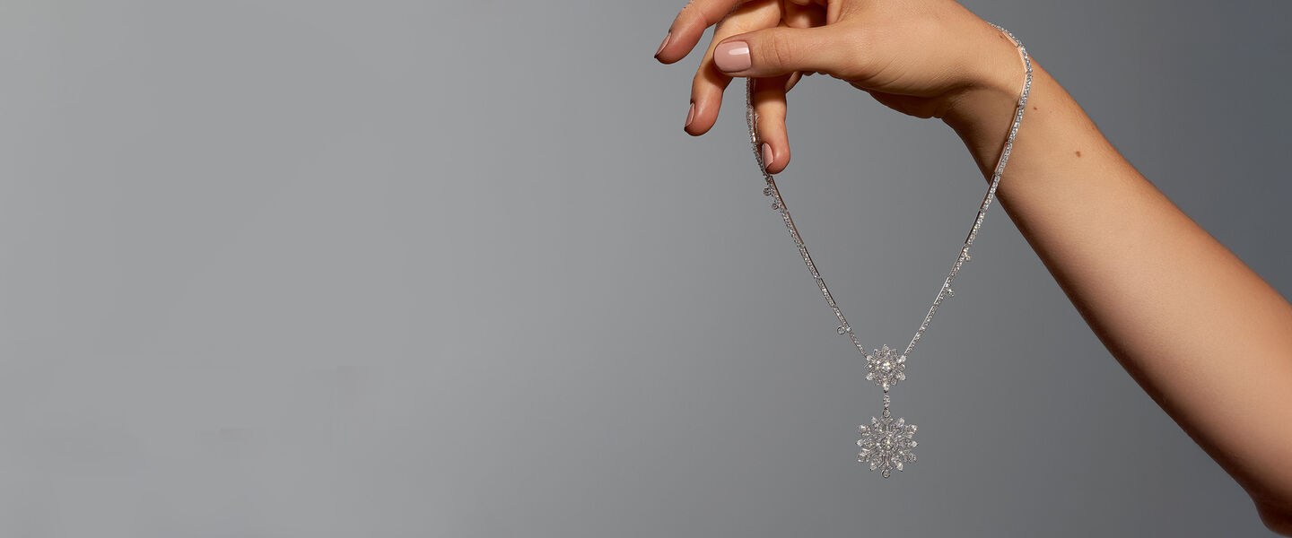 A woman holding a Birks Snowflake High Jewellery drop necklace on a grey background.