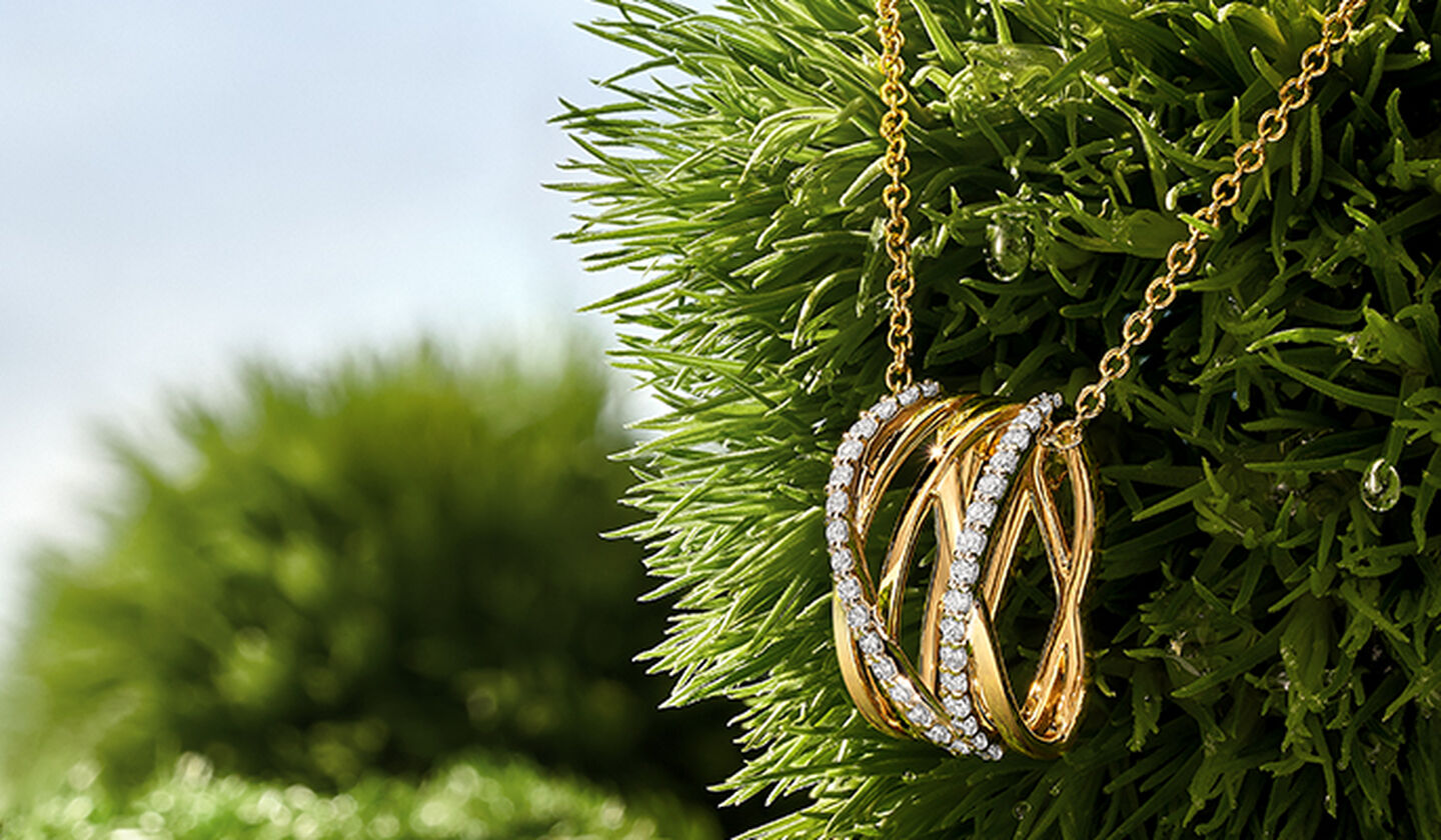 A yellow gold and diamond Rosée du Matin necklace on a green grass background