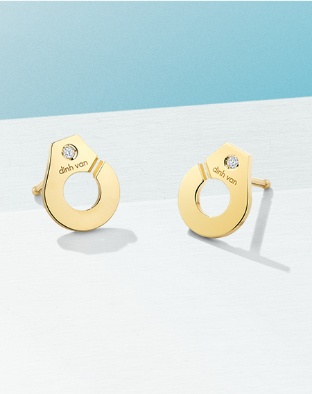 dinh van Menottes yellow gold earrings on a blue background.