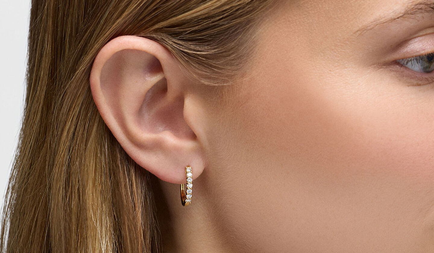 A woman wearing diamond and yellow gold Birks earrings.