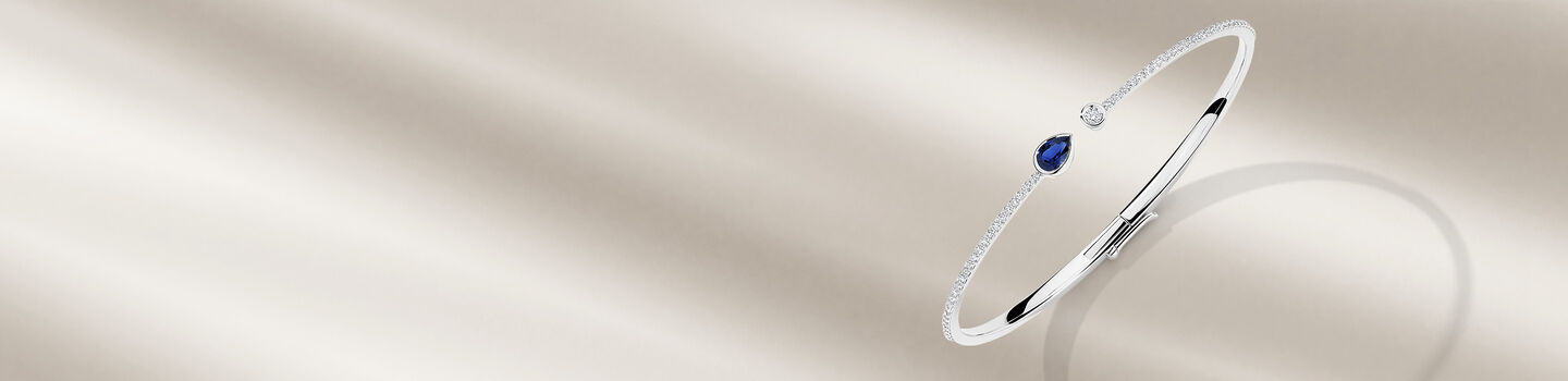 Birks Splash sapphire and diamond bangle bracelet on a beige background.