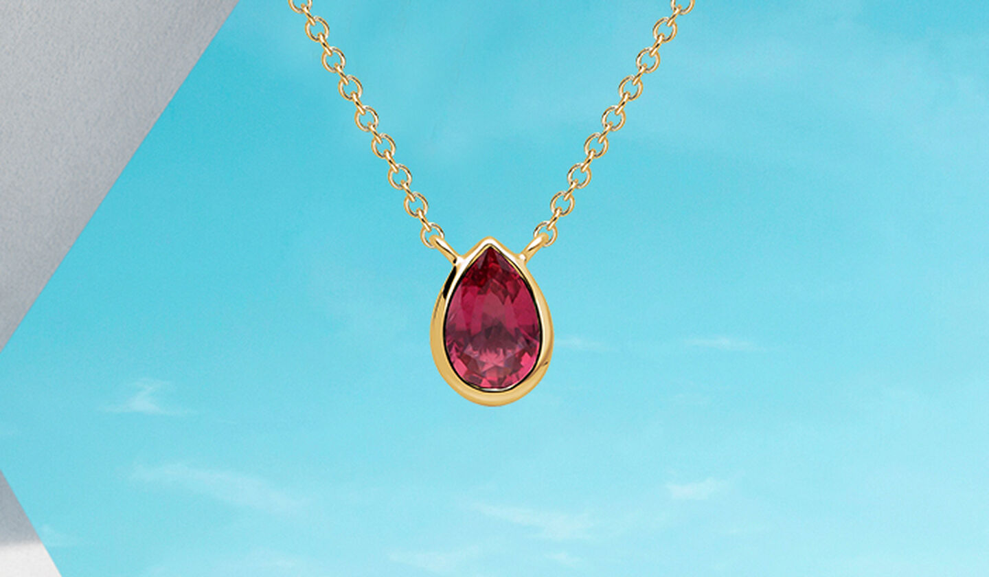 Birks Essentiels collier en or jaune avec rubis sur fond bleu.