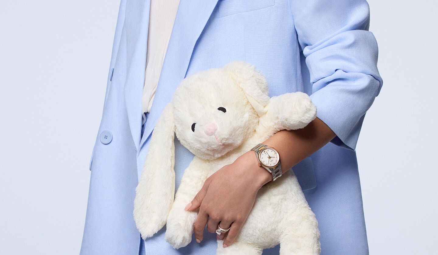 A woman holding a stuffed rabbit plush wearing a watch and jewellery from Maison Birks.
