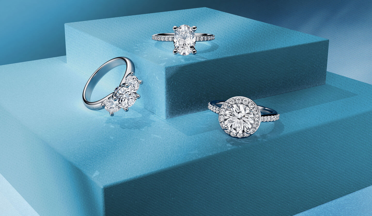 Three Birks diamond engagement rings and on a dark blue background.