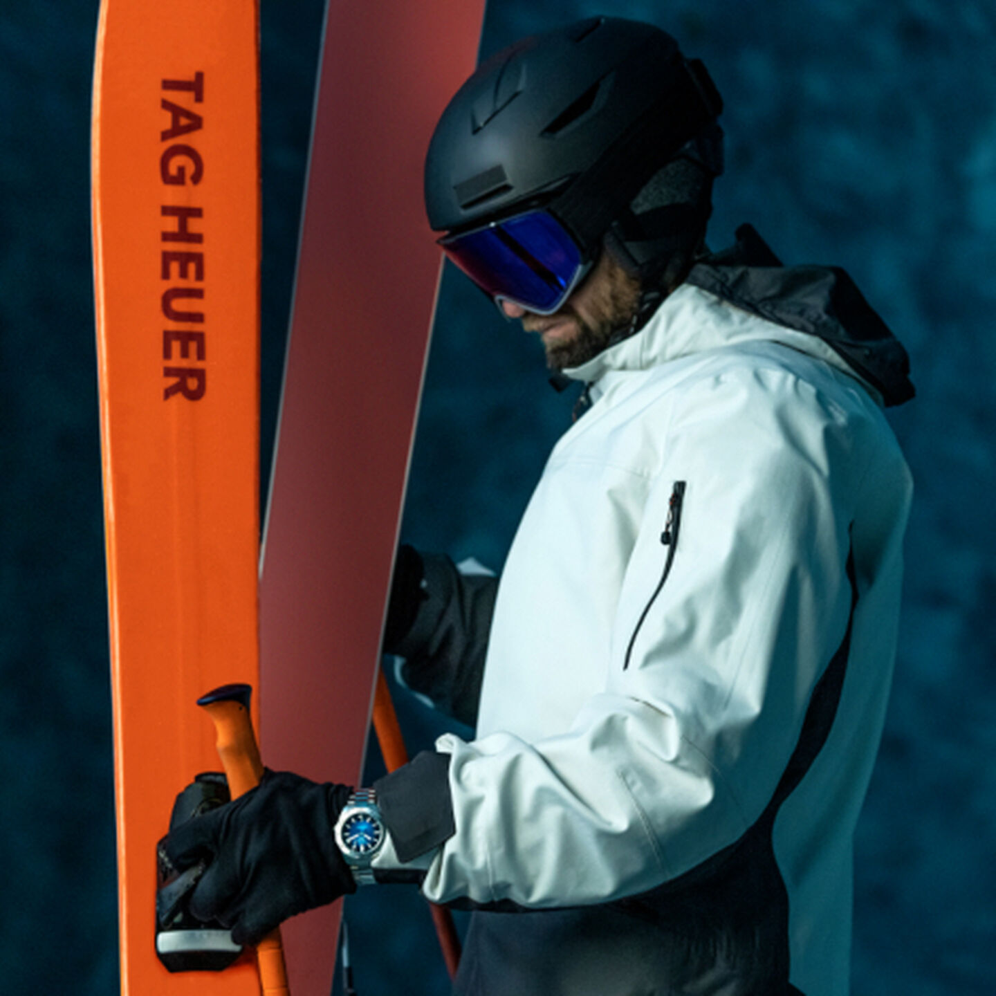 A male downhill skier pondering in a white jacket next to his orange skis