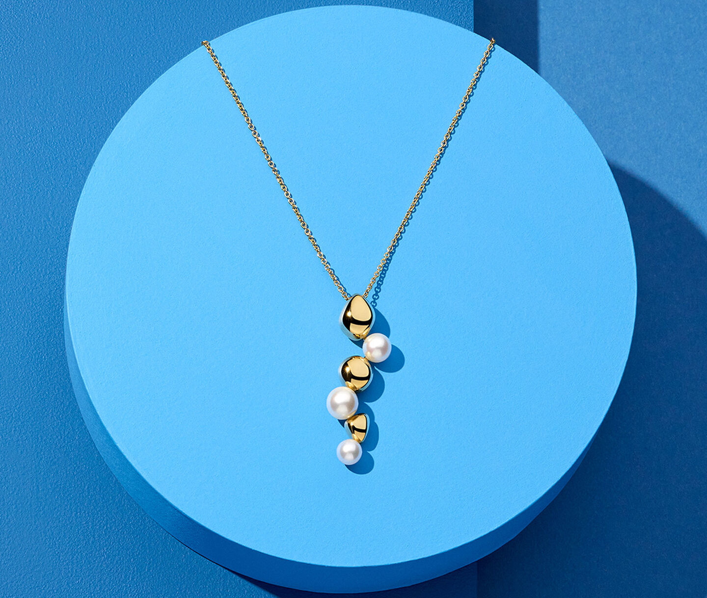 Collier Birks Pebble en or jaune et perles sur un fond bleu.